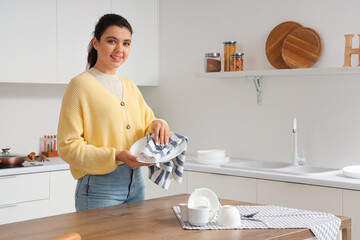 Wall Mural - Beautiful young happy woman wiping clean dishes in kitchen