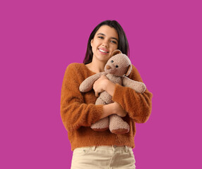 Sticker - Beautiful young happy woman hugging teddy bear on purple background