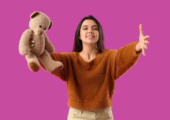 Sticker - Beautiful young happy woman with teddy bear opening arms for hug on purple background