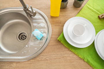 Wooden counter with sink, detergent and set of clean dishes near window in kitchen