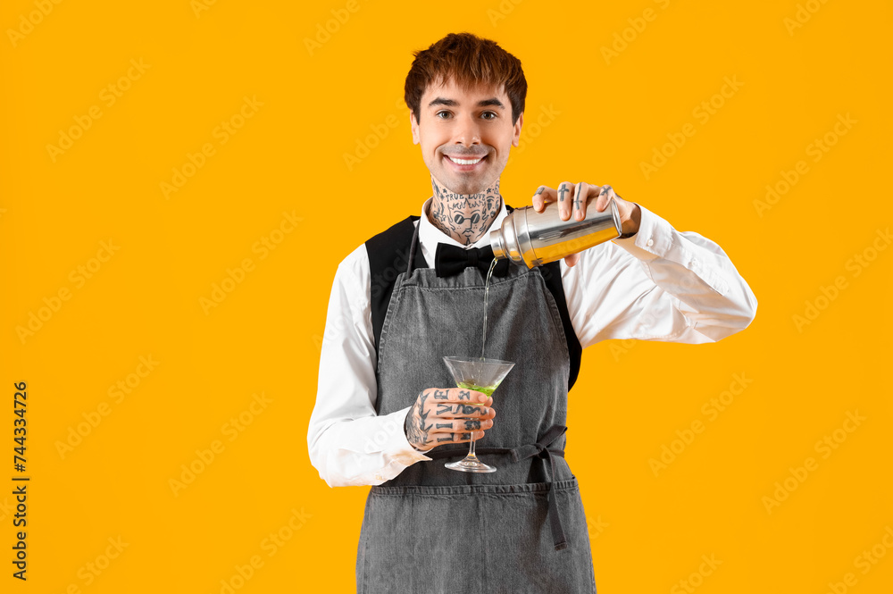Young male bartender preparing cocktail on yellow background