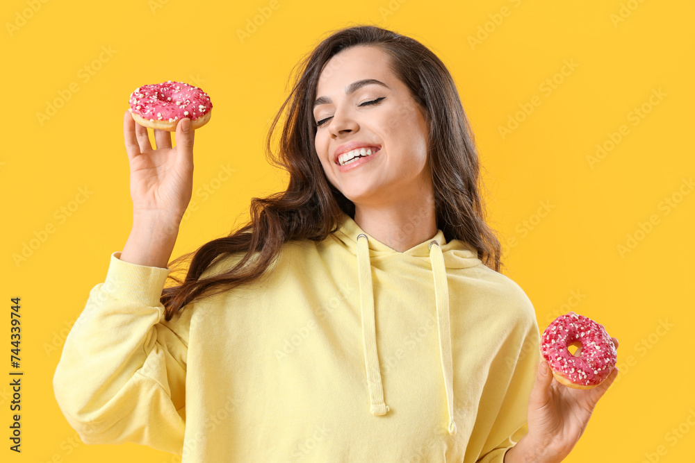 Pretty young woman with sweet donuts on yellow background