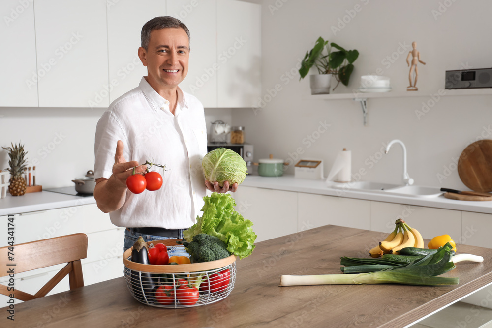 Mature man with basket of fresh vegetables at table in kitchen