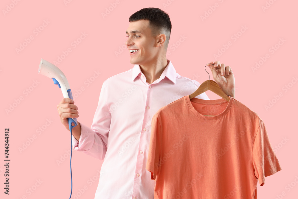 Happy young man with steamer and t-shirt on pink background