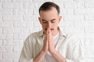 Young man praying on white brick background, closeup