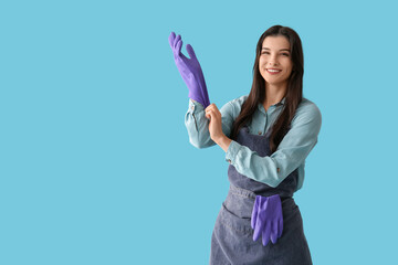 Sticker - Young woman putting on rubber gloves against blue background