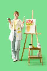 Wall Mural - Female artist with art supplies and easel on green background