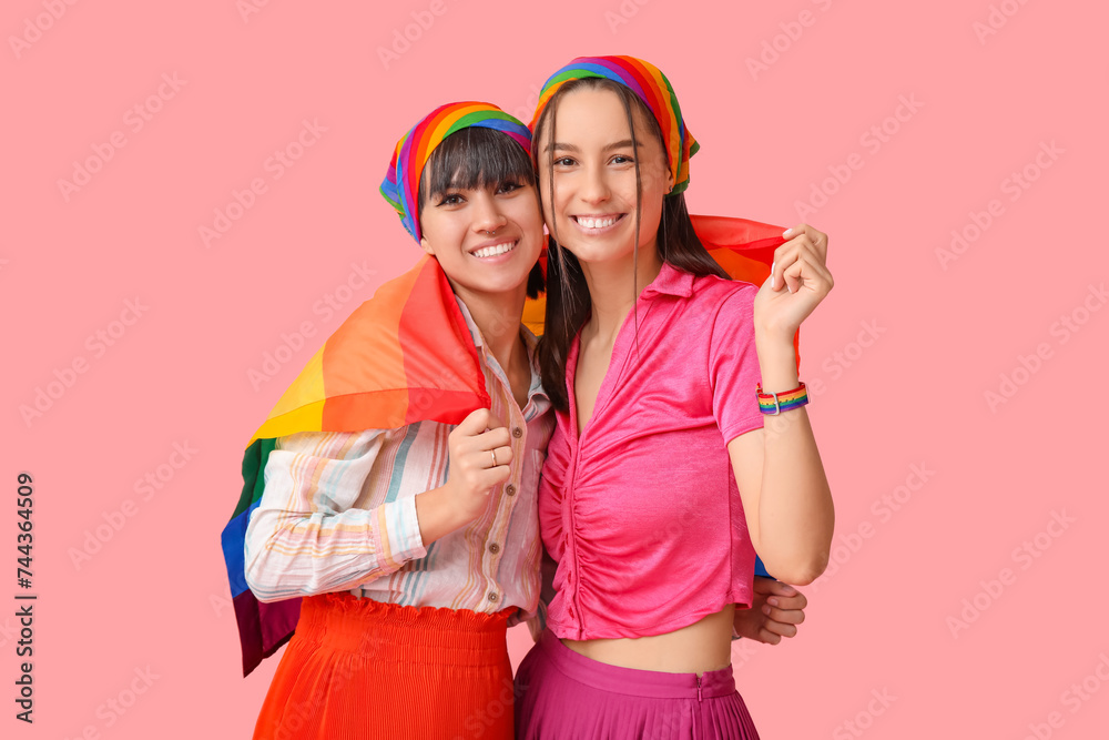 Young lesbian couple with LGBT flag on pink background