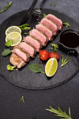 Wall Mural - sliced grilled cooked piece of tuna fillet on black stone serving board