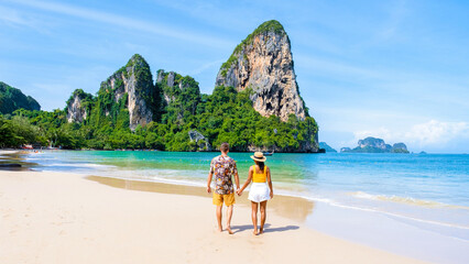 Wall Mural - a diverse couple of men and women on the beach, an Asian woman and a caucasian man walking on the beach of Railay Beach in Thailand with limestone cliffs in the background