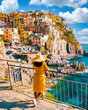 © Fokke Baarssen - Asian women visiting Manarola in Cinque Terre Italy,beautiful colorful town of La Spezia Liguria one of the five Cinque Terre, woman with hat standing by the ocean during summer in Europe