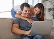 © MV/peopleimages.com - Laptop, smile and woman hugging man on sofa networking on social media, website or internet. Happy, love and female person embracing husband reading online blog with computer in living room at home.