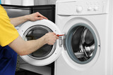 Fototapeta Kuchnia - Plumber repairing washing machine with screwdriver indoors, closeup