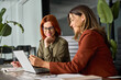 © insta_photos - Two happy busy female employees working together using computer planning project. Middle aged professional business woman consulting teaching young employee looking at laptop sitting at desk in office