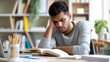 © HelenP - A man appears fatigued as he rests his head in his hand while studying at a desk with open books, suggesting exhaustion or frustration during a study session.