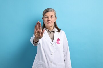 Poster - Mammologist with pink ribbon showing stop gesture on light blue background. Breast cancer awareness