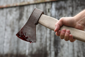 Man holding bloody axe outdoors, closeup view