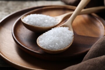 Organic salt in spoons on wooden table, closeup