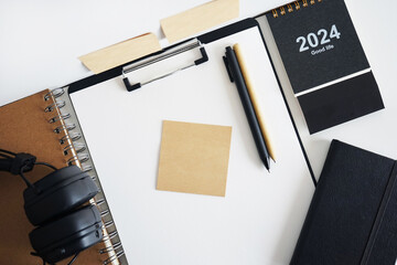 Clip folder with paper next to notepads, calendar, stickers, pens and black headphones on white background