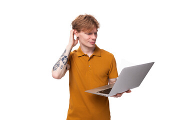 young red-haired guy in an orange t-shirt is studying using a laptop on a white background with copy space