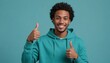 A cheerful man in a teal hoodie giving double thumbs up. His relaxed posture and casual wear suggest comfort and a friendly vibe.