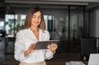 © Stock 4 You - Latin Hispanic mature adult professional business woman looking at online trade app. European businesswoman CEO holding digital tablet using fintech tab application standing at workplace in office.