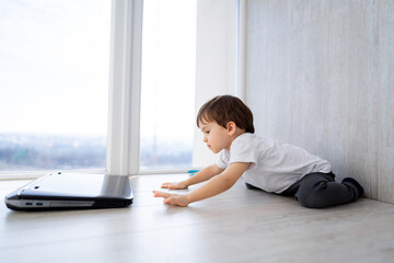 Wall Mural - Little boy is sitting on the floor and playing with laptop.