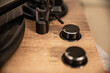 This is a detailed image of a section of a wooden turntable, focusing on its control knobs and part of the tonearm. Two black knobs are visible, likely for speed control, as indicated by the numbers 