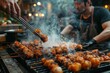 A man expertly grills a mouth-watering mix of churrasco, yakitori, and kebabs on an outdoor barbecue, adding a sizzling touch to his street food dishes with the flick of his tongs