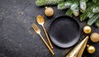 christmas table setting with empty black ceramic plate fir tree branch and gold accessories on black stone background top view copy space