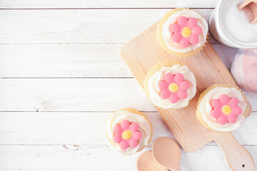 Poster - Pink spring flower cupcakes on a serving platter. Top down view table scene with a white wood background. Copy space.