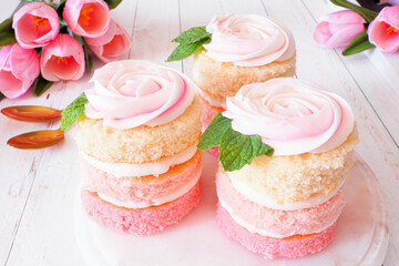 Poster - Spring mini cakes with buttercream rose. Table scene with a white wood background. Pink layers with flower topping.