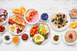 Healthy breakfast or brunch table scene on a white wood background. Top down view. Avocado toast, smoothie bowls, oats, yogurt and a variety of nutritious foods.