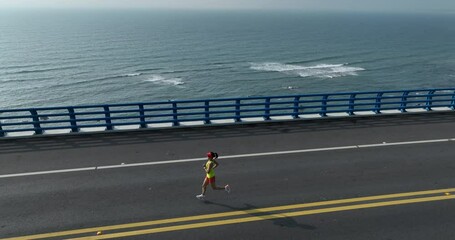 Poster - Aerial footage of woman running on sunrise seaside bridge