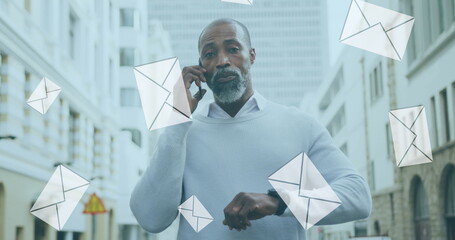 Wall Mural - Image of digital mail envelope icons over african american man using smartphone in city