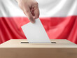 Voter's hand submitting a ballot into a clear box, with a crisp Poland flag backdrop, a symbol of electoral process