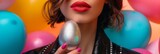 Fototapeta  - a brunette with red lipstick is holding a silver easter egg, she is standing in front of a background of colorful balloons.