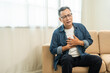 © Chanakon - Old man senior he felt a pain in his chest held his hand and squeezed it. Mature Heart attack that needed treatment. Sitting on sofa couch in living room at house