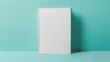 A blank hardcover book mockup standing against a light blue and green background, perfect for showcasing designs or illustrations