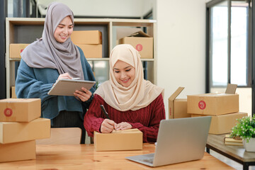 Friend muslim female two work business sme online shopping working on laptop computer with parcel box on desk at home, SME online business and delivery concept