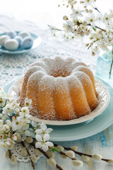 Wall Mural - Bundt cake, Babka sprinkled with powdered sugar on a festive table decorated with spring flowers, close up view. Easter pastry