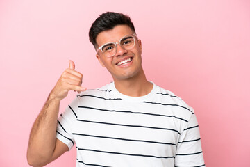 Wall Mural - Young caucasian handsome man isolated on pink background With glasses and doing phone gesture