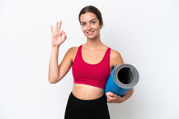 Wall Mural - Young sport caucasian woman going to yoga classes while holding a mat isolated on white background showing ok sign with fingers