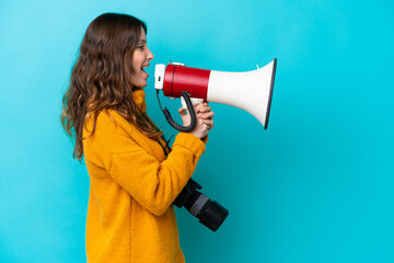 Wall Mural - Young photographer woman isolated on blue background shouting through a megaphone