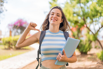 Sticker - Young pretty student woman at outdoors proud and self-satisfied