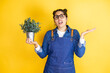 Young caucasian gardener woman holding a plant isolated on yellow background clueless and confused expression with arms and hands raised