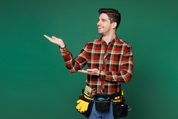 Wall Mural - Young employee laborer handyman man wear red shirt point hands arms finger aside on area isolated on plain green background. Instruments accessories for renovation apartment room. Repair home concept.