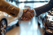 Two people shaking hands in car dealership. Close-up shot with bokeh lights background.