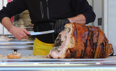 Wall Mural - hand with black glove of a deli worker slices roasted porchetta with a large knife