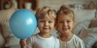 Adorable toddler siblings embrace, holding a balloon, enjoying a playful indoor birthday celebration.